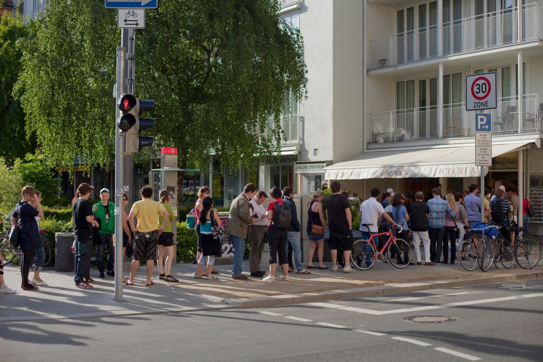Busy street scene with pedestrians and cyclists outside an ice cream shop in Munich.
