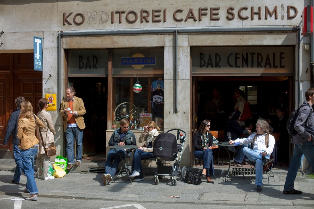 Exterior of Bar Centrale café in Munich with seated patrons and passersby on the street.