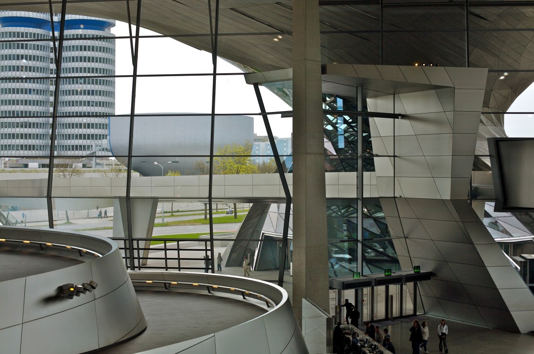Interior of BMW Welt with modern architecture, large windows overlooking BMW towers and museum building.