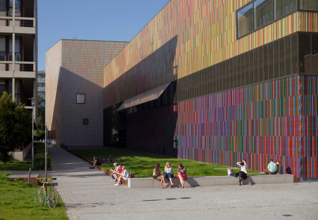 Modern museum building with colorful vertical striped facade and people sitting on lawn