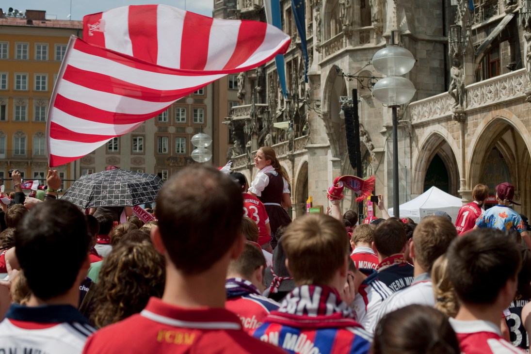 FC Bayern Munich fans celebrating in Marienplatz with red and white striped flag.