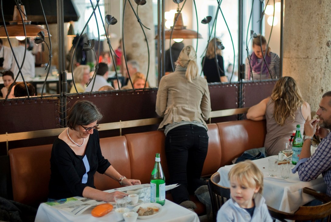 Sunday brunch diners seated at tables in a modern restaurant with brown leather booths and pendant lighting.