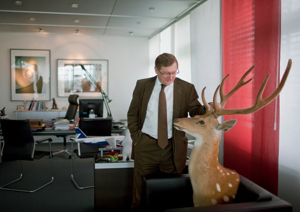 Man in business suit standing next to a mounted deer head with large antlers in an office.