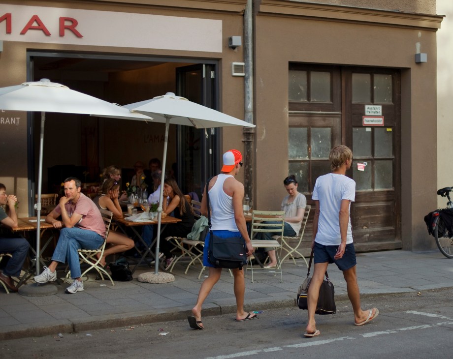 Outdoor café with white umbrellas and diners, runners jogging past on street