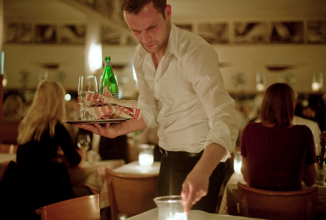 A waiter in a white shirt serves food on a plate at Kull restaurant in Munich.