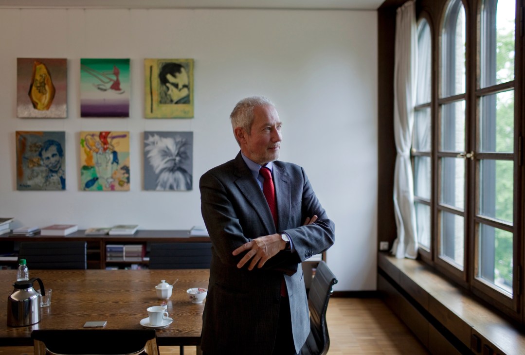 Klaus Schrenk, director of the Pinakothek der Moderne museum, stands in an office with colorful artworks on the wall behind him.