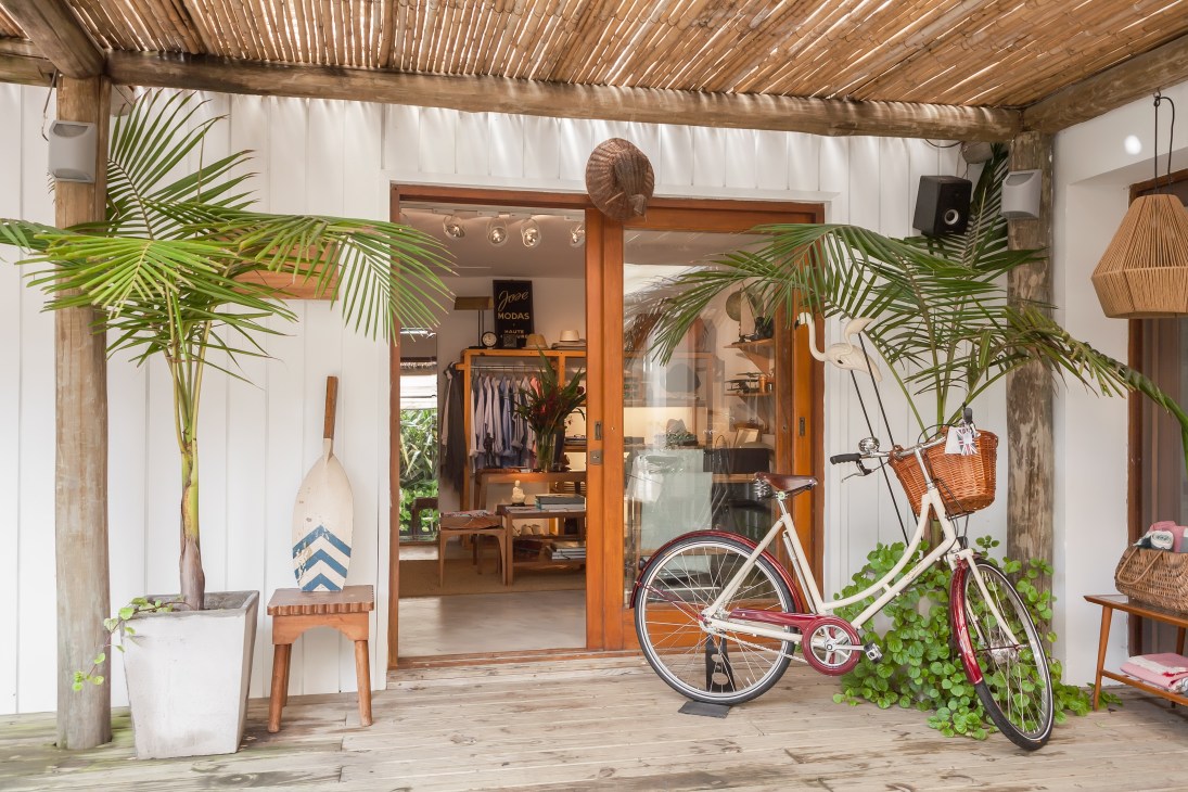 Entrance to Mutate boutique with wooden doors, potted palms, a red bicycle, and eclectic retail items displayed.