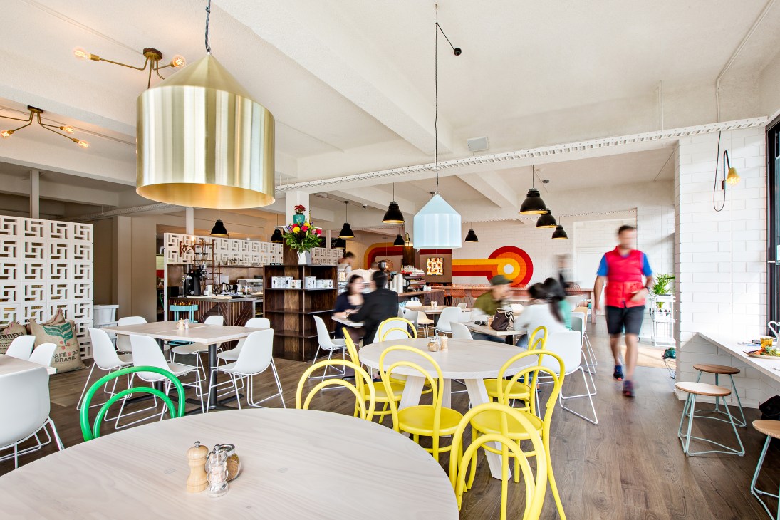 Modern café interior with yellow chairs, brass pendant lighting, and geometric wall patterns at My Kingdom for a Horse in Adelaide.