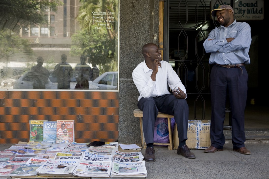 A Nairobi newspaper vendor and customer at a street stall with newspapers and magazines displayed.