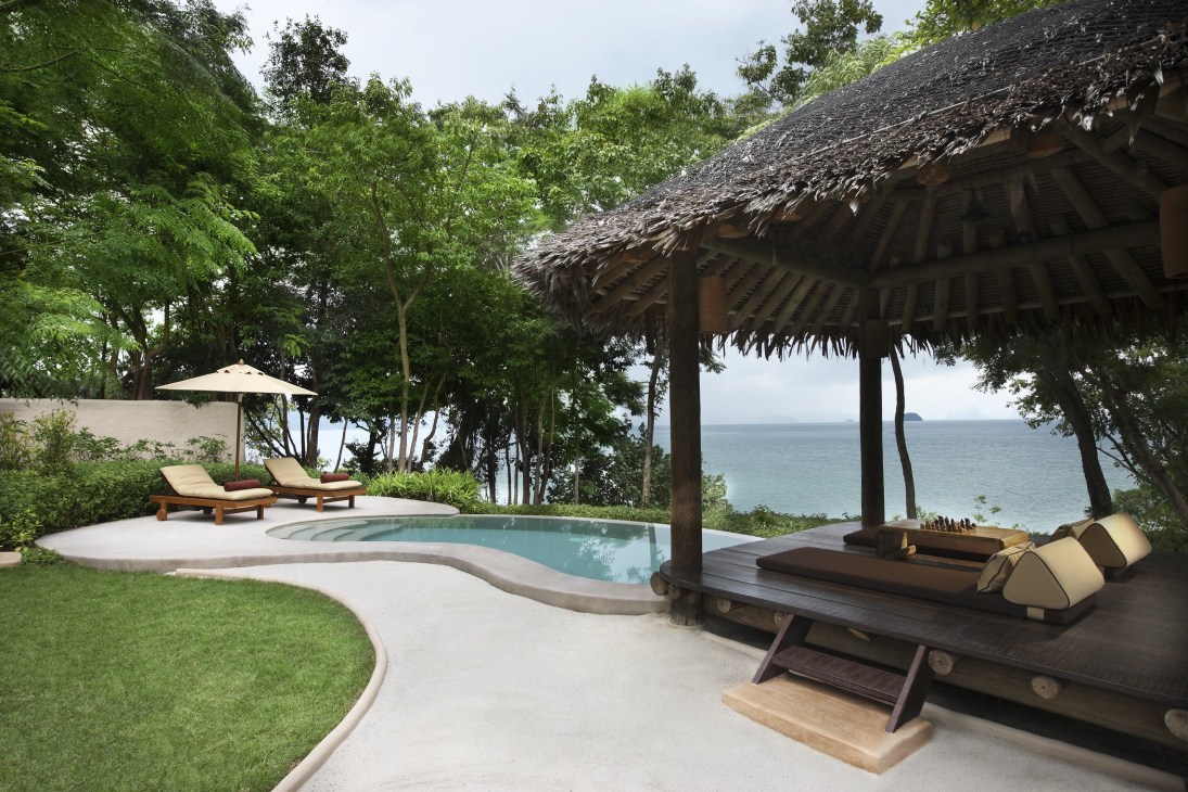 Tropical villa with thatched roof, pool, and lounge chairs overlooking the Andaman Sea at Naka Island, Phuket.