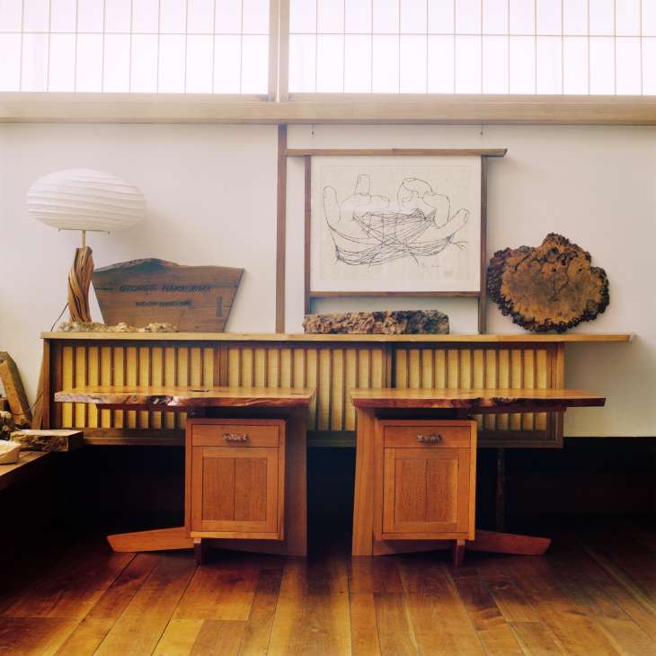 Two wooden cantilevered night stands with cherry wood tops displayed in a showroom with sketches and objects on the wall above.