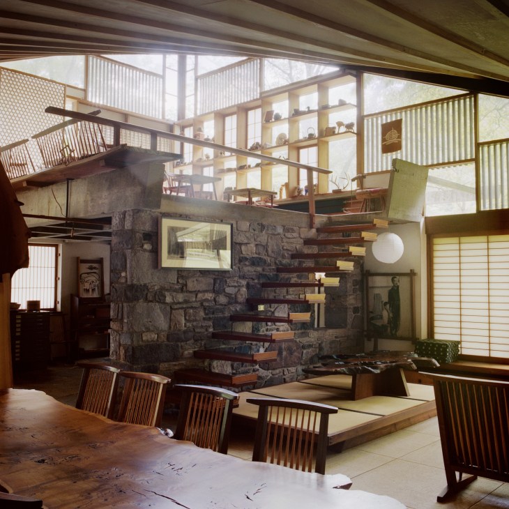 Interior of Nakashima Woodworker's arts building with stone fireplace, wooden furniture, and large windows.