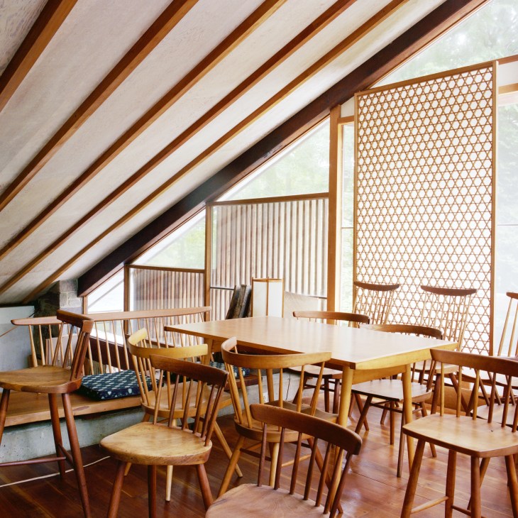 Lofted interior space with wooden chairs and tables displayed under exposed beam ceiling and geometric wooden screens.