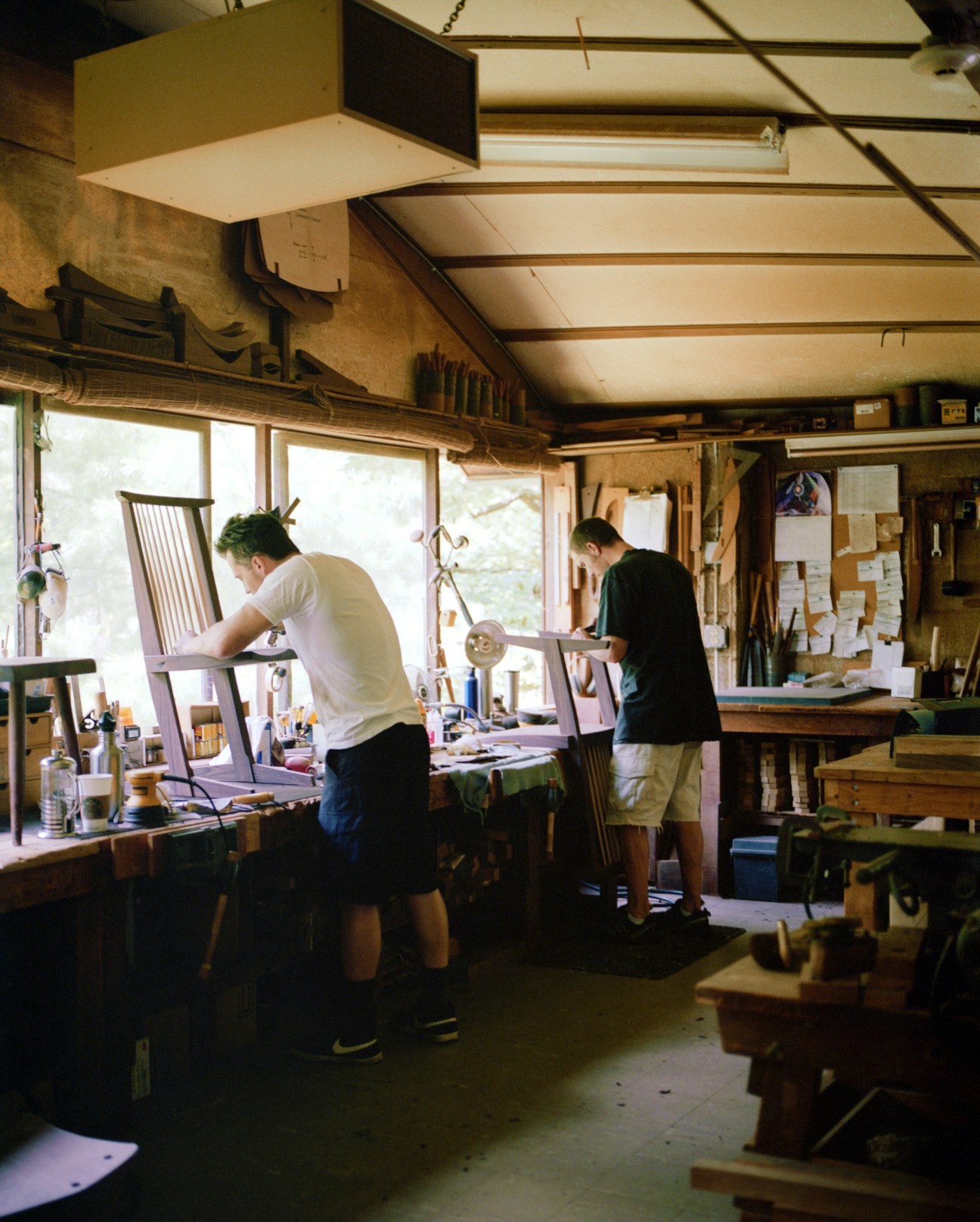 Two woodworkers assembling wooden chairs in a bright, naturally lit workshop at Nakashima Woodworker.