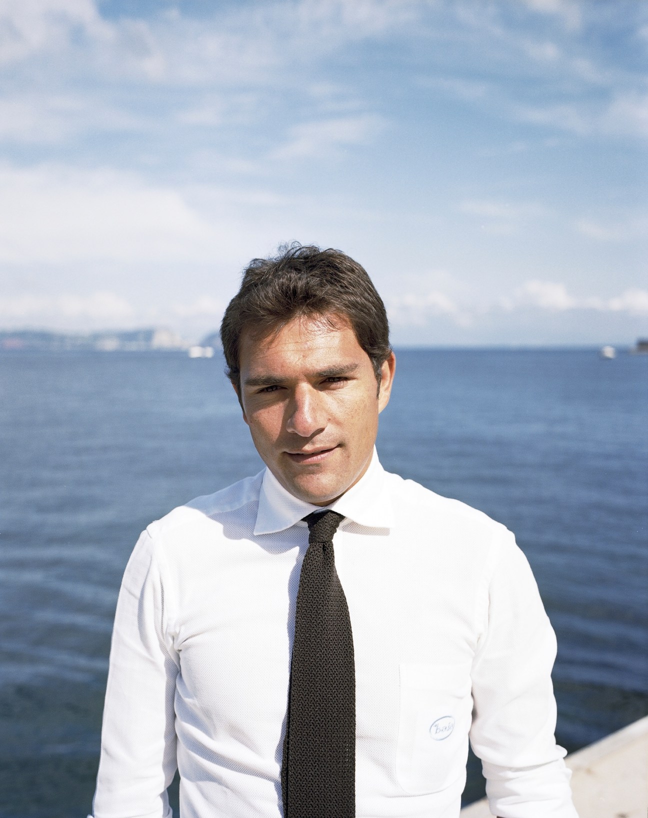 Roy Capasso of Baia boats standing in white shirt and tie with Naples bay in background