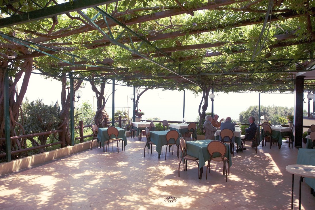 Vine-covered terrace at Ristorante Rosiello with tables, chairs and bay views.