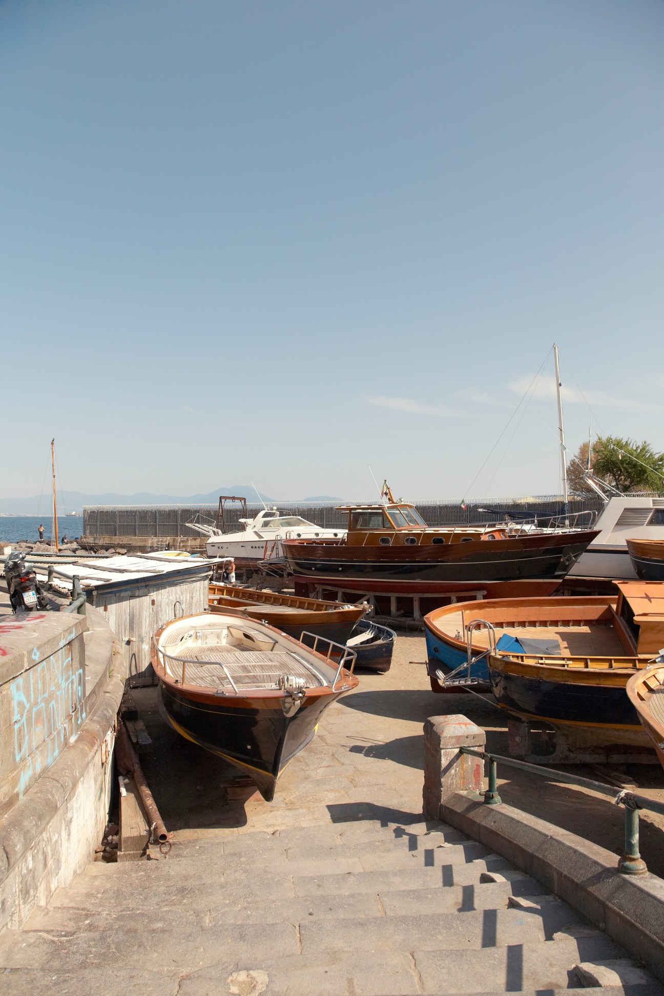 Traditional wooden fishing boats moored at a Naples marina with Vesuvius visible across the bay.