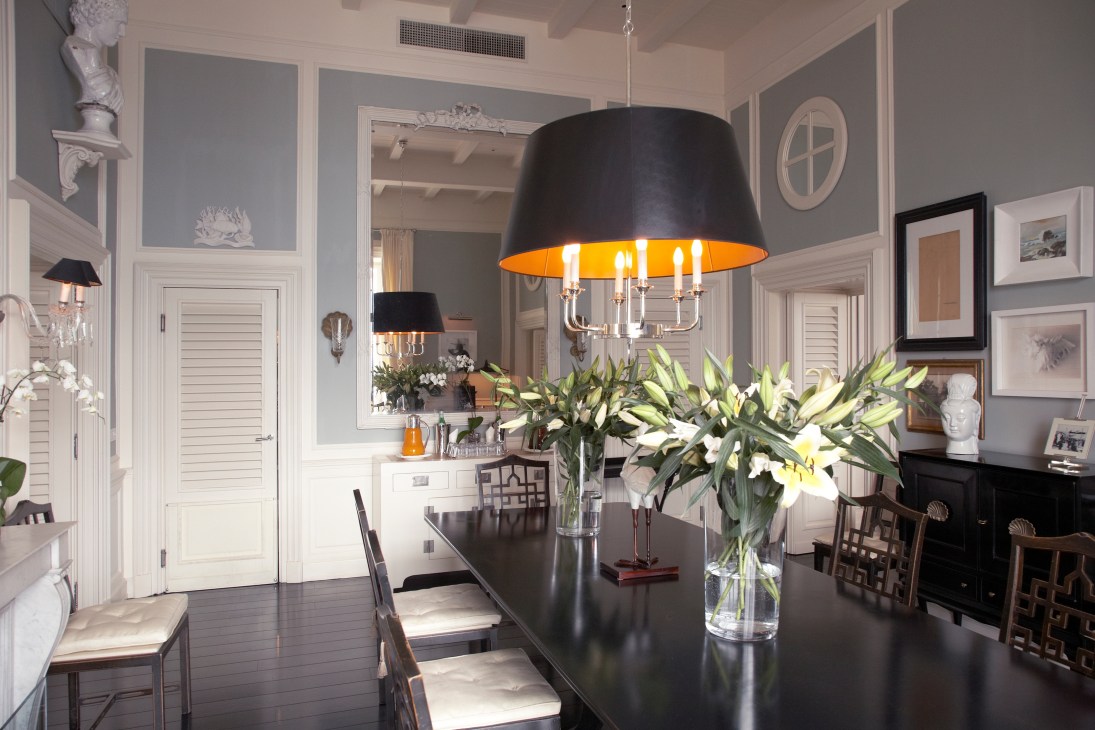 Elegant reception room with high ceilings, white paneling, black dining table, and modern black pendant lamp with gold interior.
