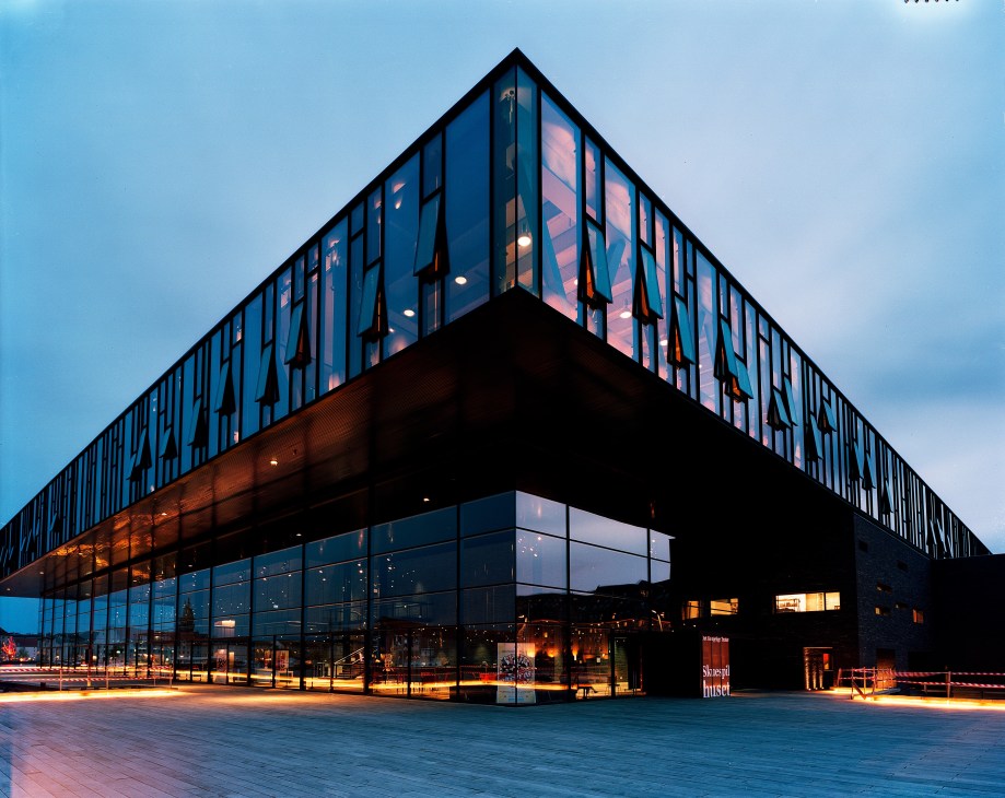 Copenhagen's National Theatre exterior at dusk with illuminated glass and dark facade.