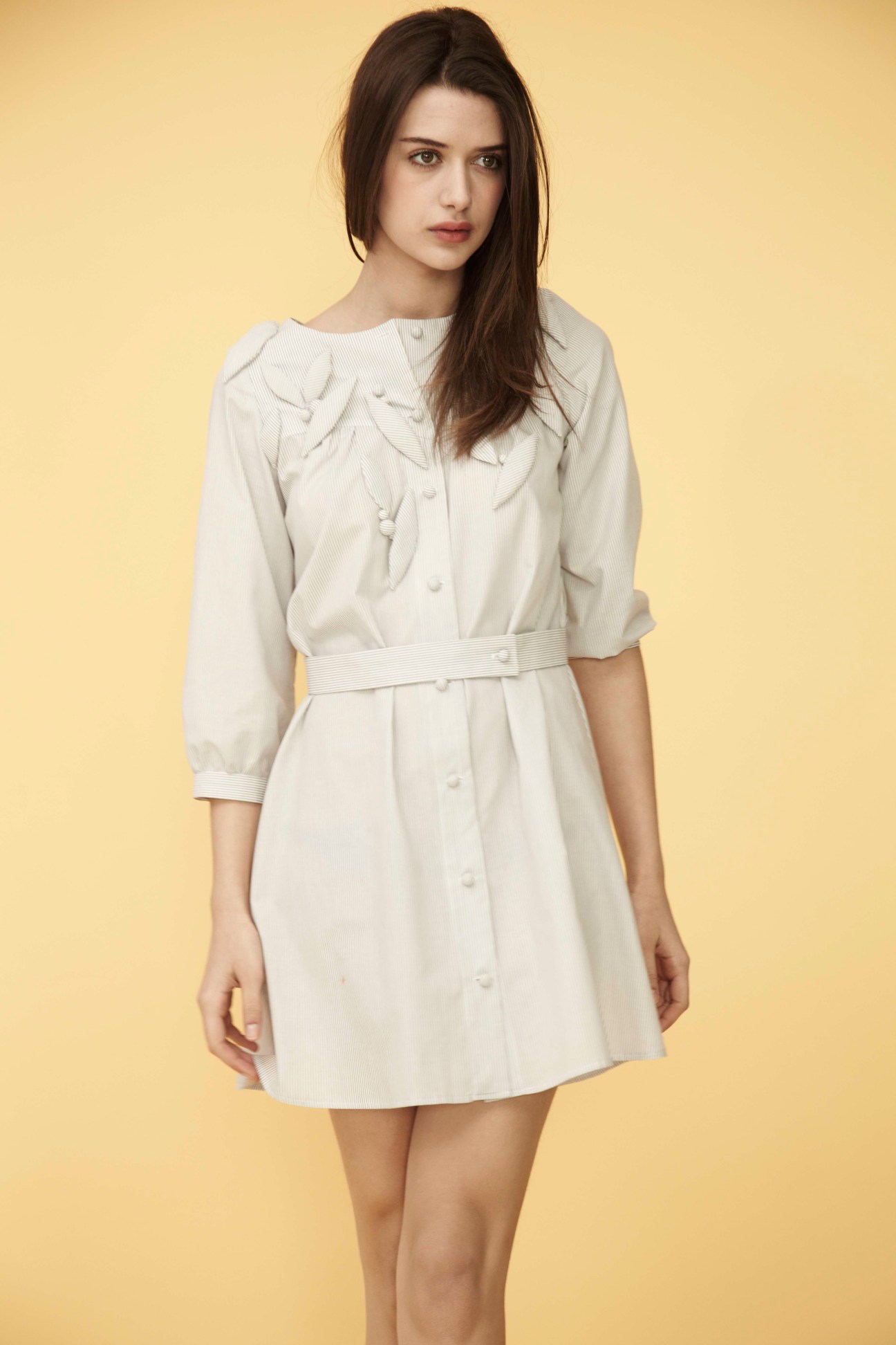 Woman wearing a cream-colored button-front dress with leaf and berry print details against a yellow background.