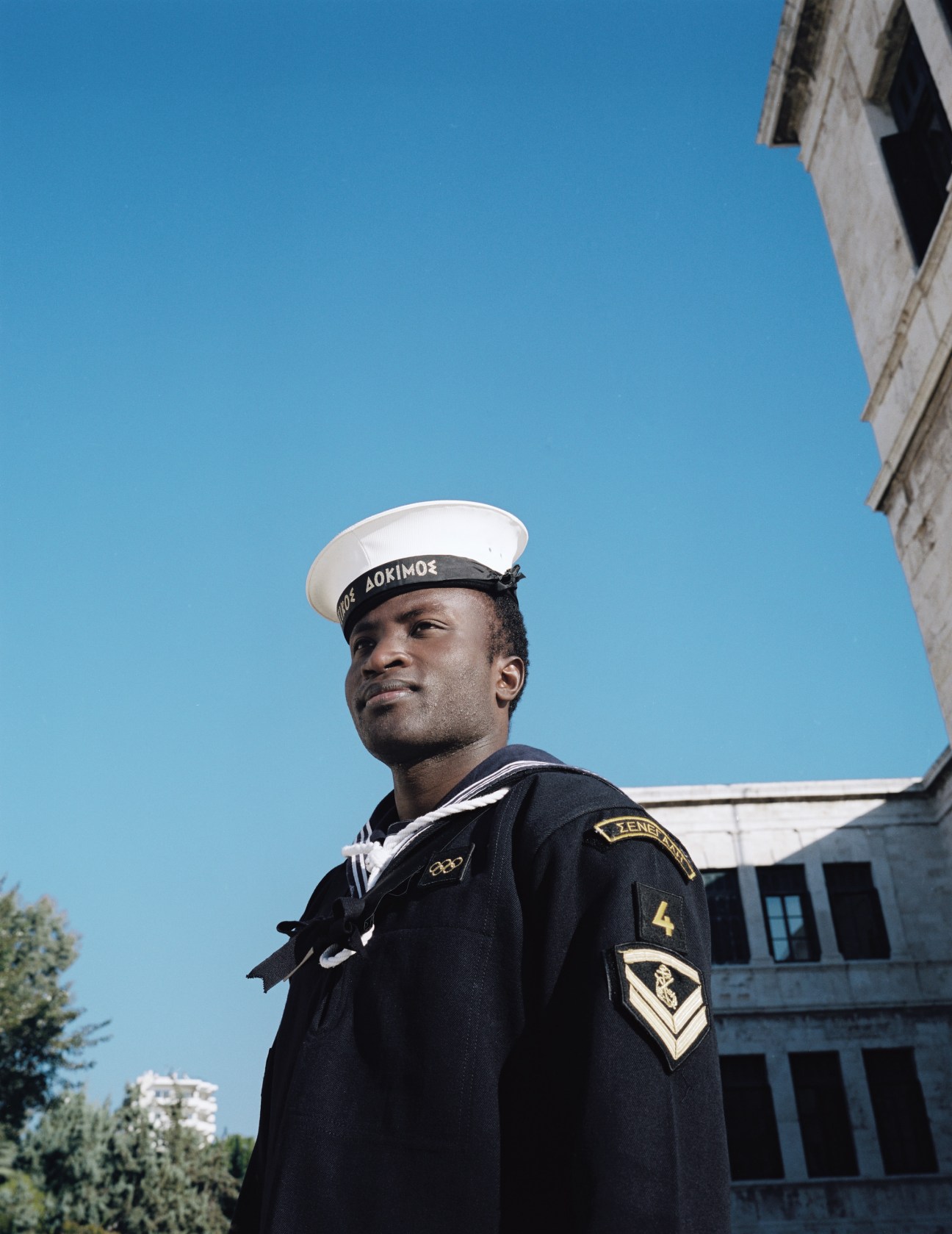 Seydouna Hamza Amar in navy sailor uniform stands against a clear blue sky.