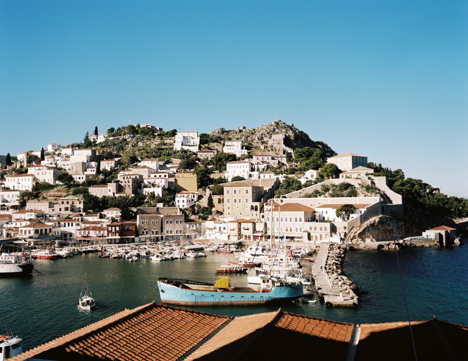 Hydra island harbour with white-washed buildings cascading down hillside and fishing boats in turquoise waters.