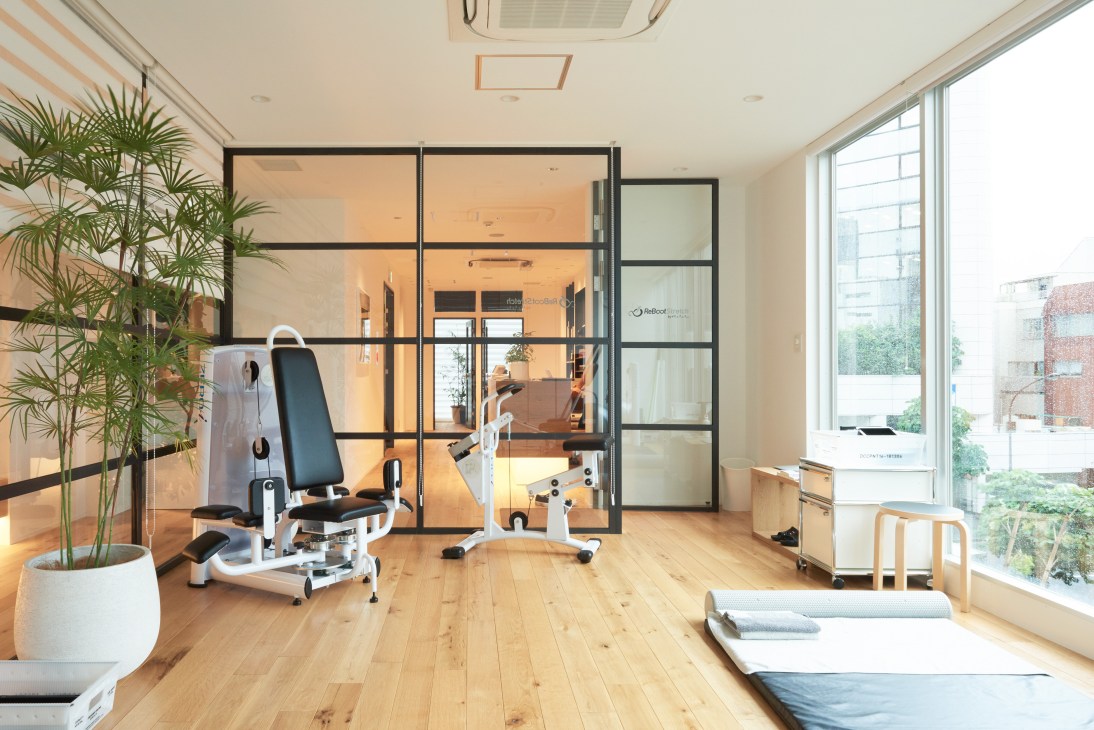 Modern fitness studio with wooden flooring, exercise equipment, potted plants, and floor-to-ceiling windows at Neutralworks Tokyo.