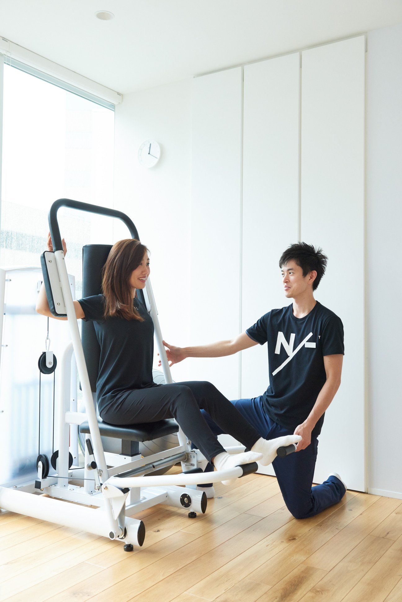 A trainer assists a client using exercise equipment at Neutralworks Tokyo fitness studio.