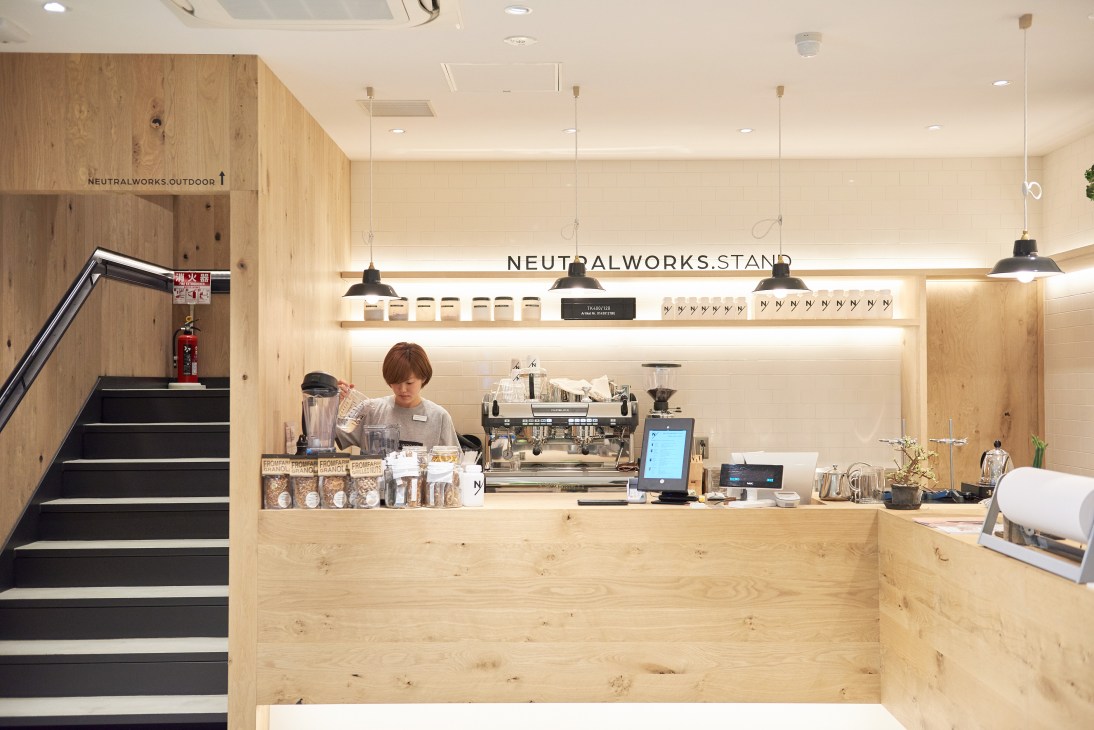 Neutralworks Tokyo café counter with staff member, wooden interior, and signage.