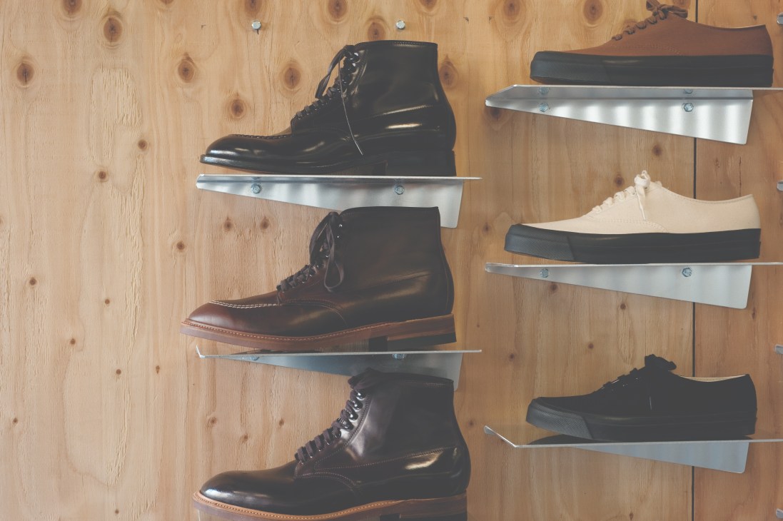 Lace-up boots and shoes displayed on metal shelves against a wooden wall at Anatomica Tokyo.
