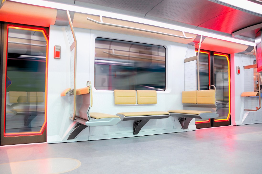 Interior of Warsaw's Inspiro metro train car designed by DesignworksUSA, featuring yellow seating, red-framed doors, and wooden handrails.