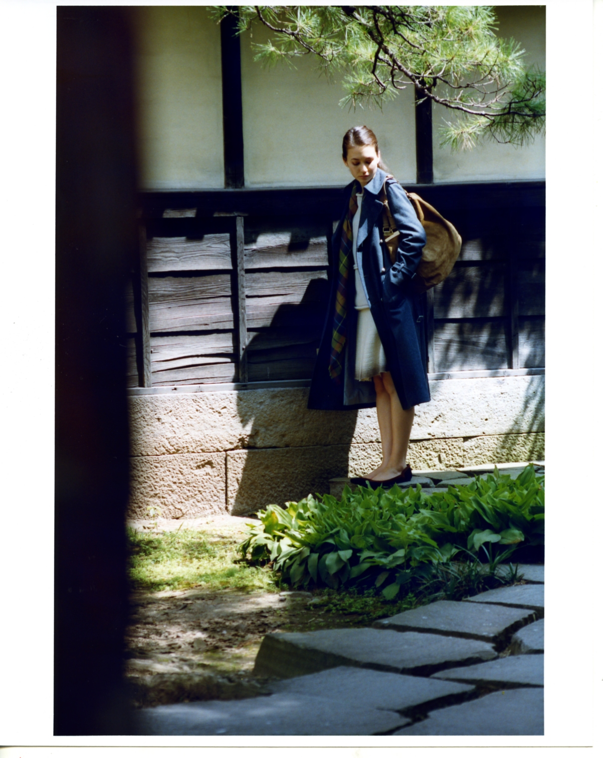 Model wearing a navy Drawer coat over a Bottega Veneta top and skirt in a traditional Japanese courtyard garden.