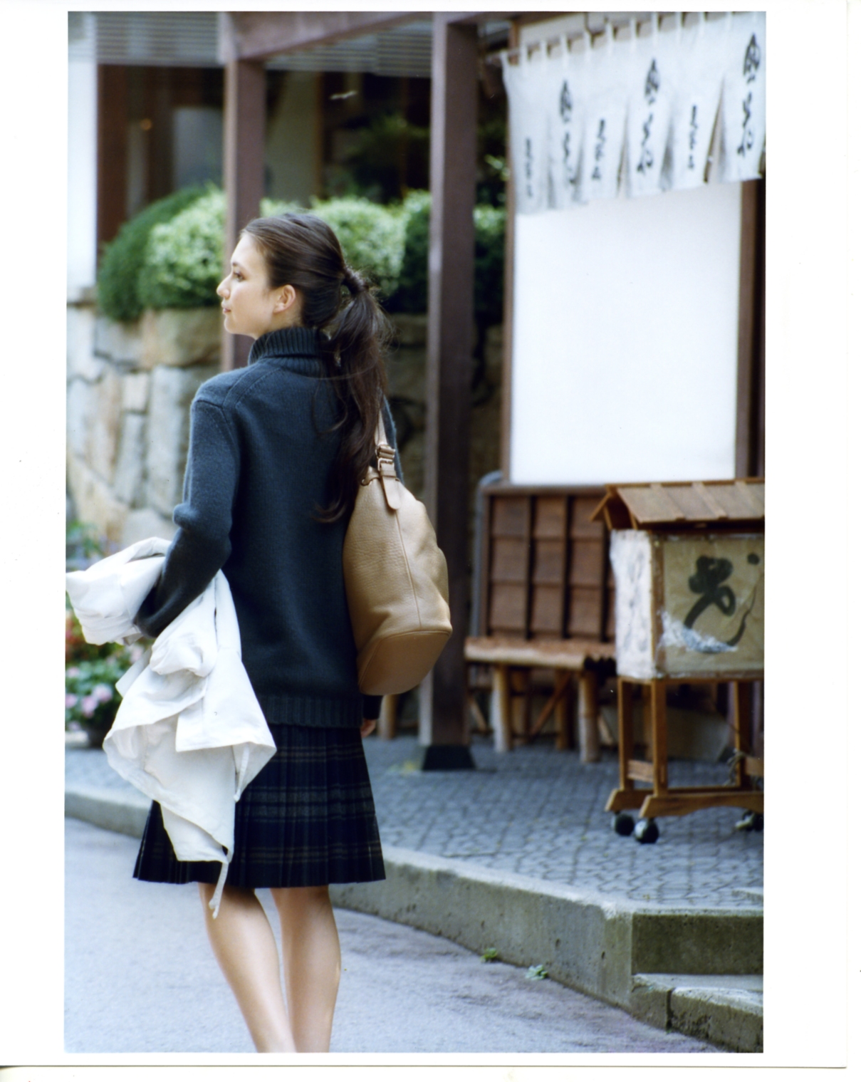 Woman wearing navy Drawer jumper and Prada skirt walking past traditional Japanese storefront in Obuse.