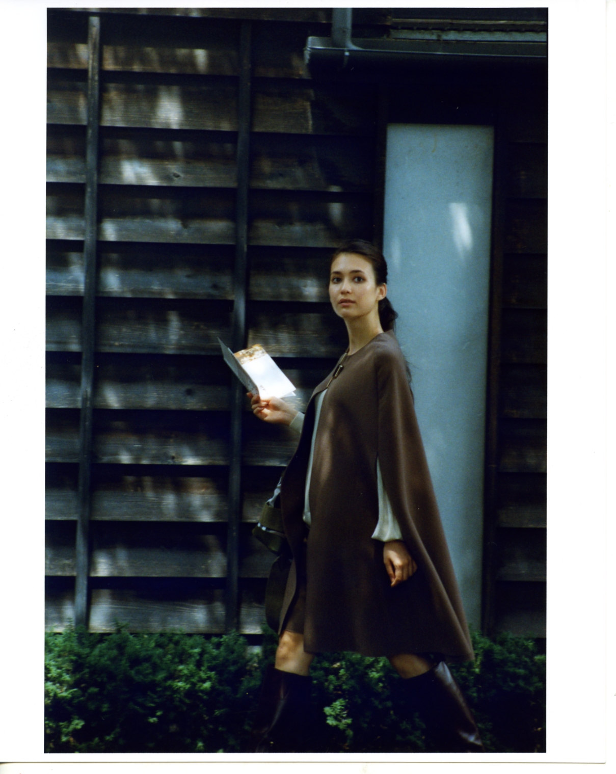 Woman wearing a brown Lanvin coat and skirt with Drawer blouse and Burberry boots and bag, standing against a wooden structure in Obuse.