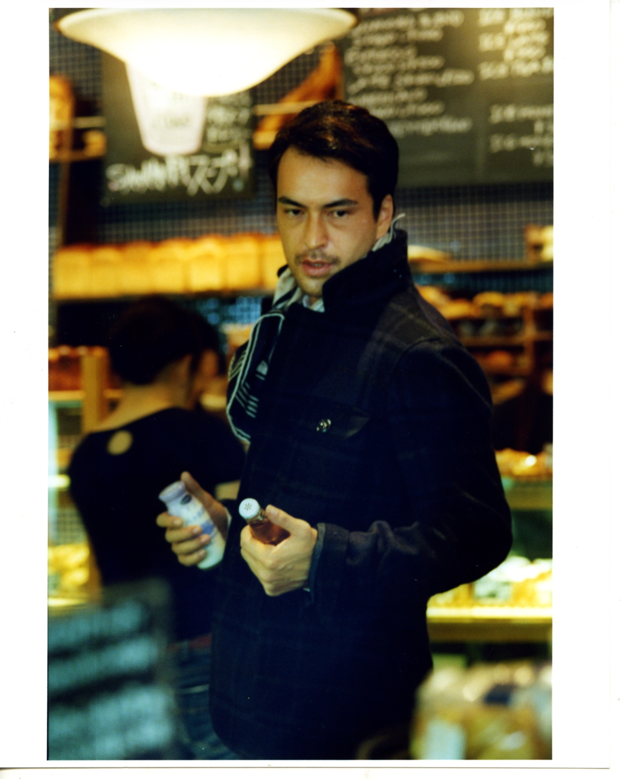 Man wearing Woolrich John Rich & Bros jacket and Hermès scarf in a café setting.