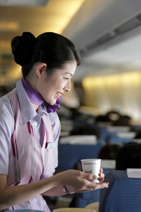 ANA flight attendant in purple scarf serving beverage with professional smile.