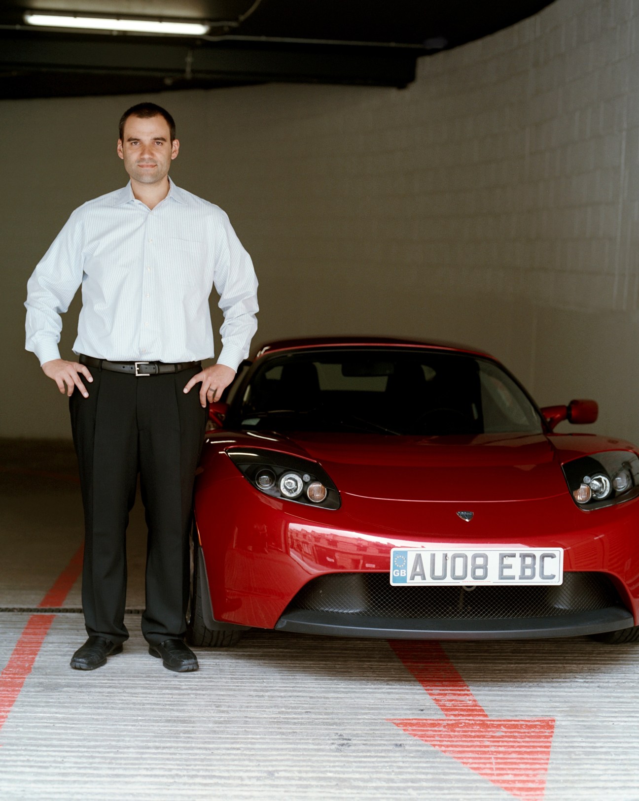 Darryl Siry, Tesla senior vice president, stands next to a red Tesla Roadster sports car in a garage.