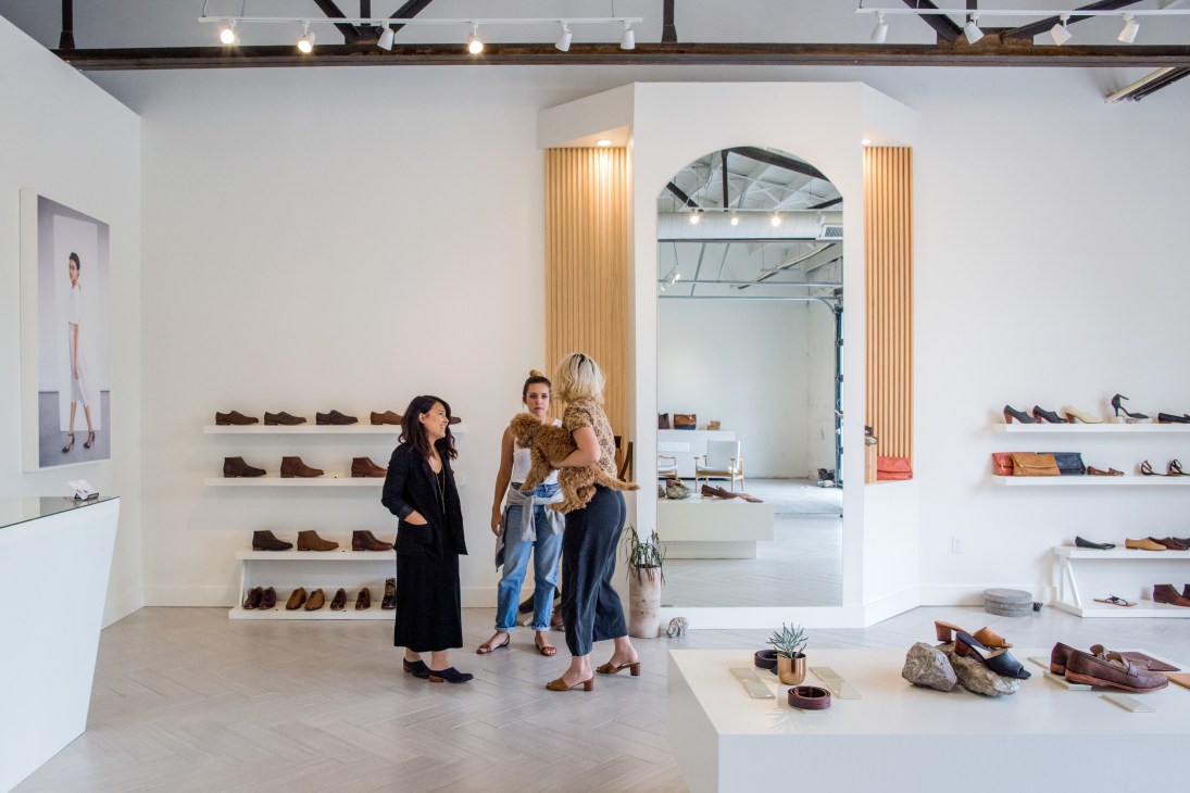 Interior of Nisolo shoe shop in Germantown with customers browsing handcrafted footwear displayed on white shelves.