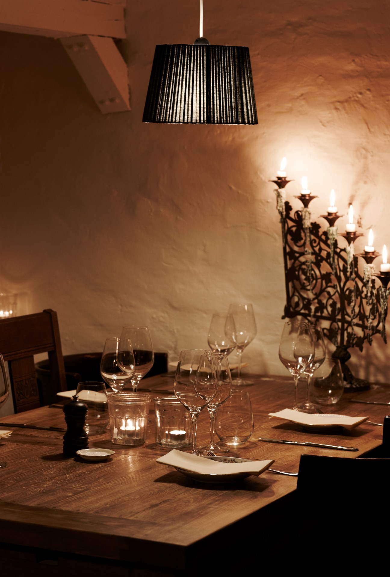 A restaurant dining table set with glasses, place settings and a decorative pendant lamp overhead.