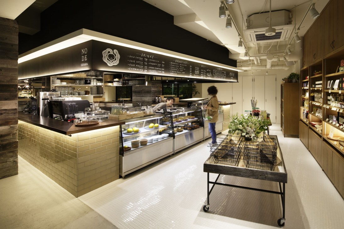 Modern café interior with counter service, menu board, and retail shelving at Node Uehara in Tokyo.