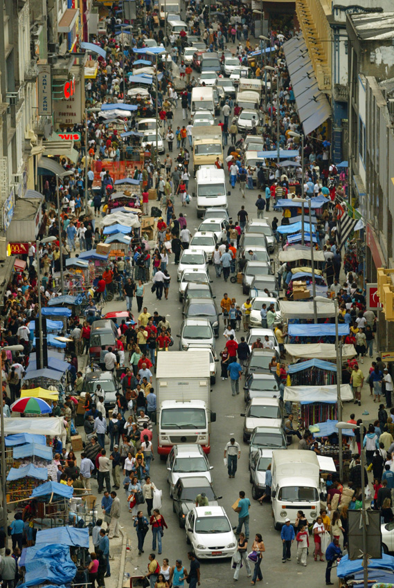 Aerial view of a crowded street market with vendors, umbrellas, and vehicles in an urban area.