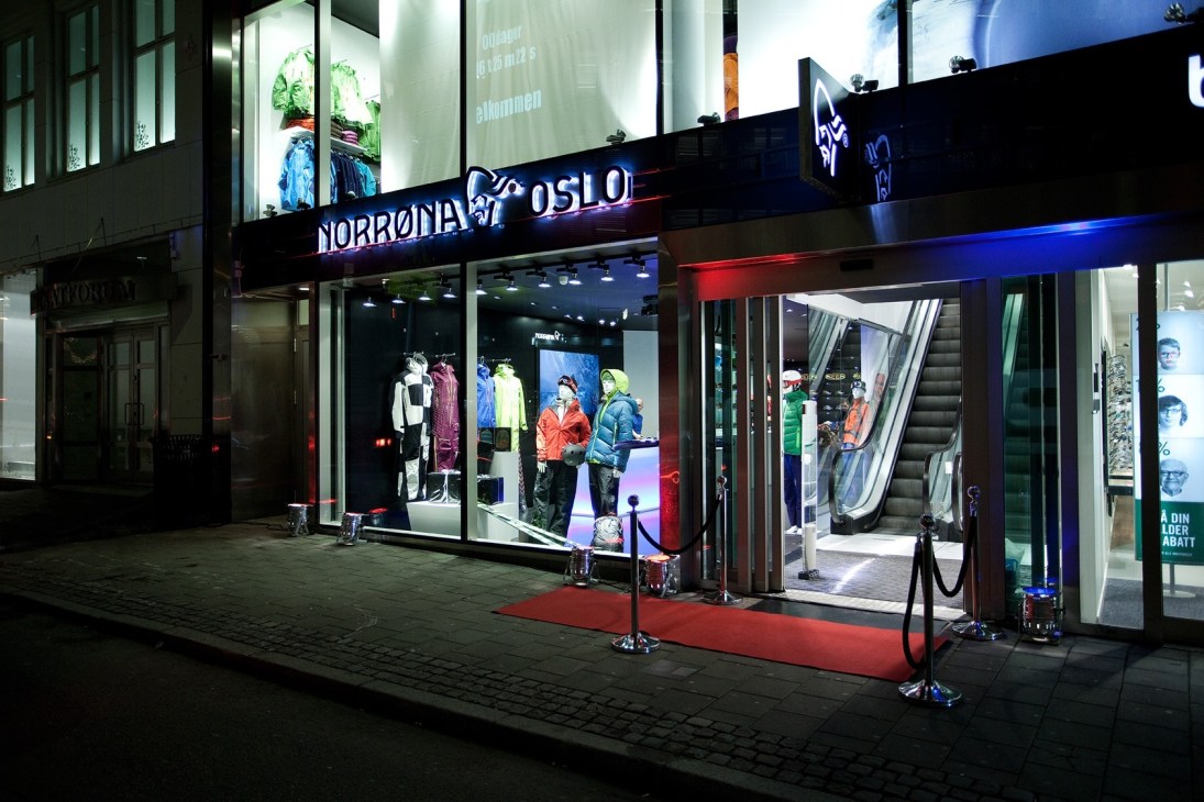 Norrøna's first retail store in Oslo at night, featuring a black storefront with illuminated signage and colorful outerwear displayed in windows.