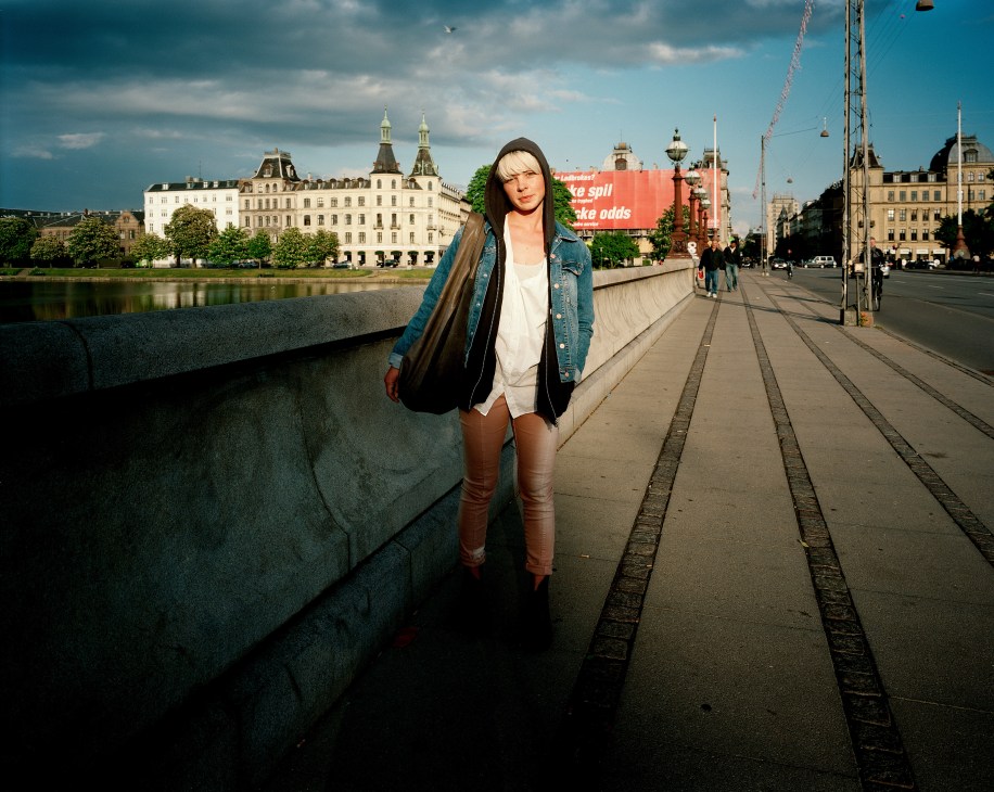Woman in denim jacket standing on Queen Louise bridge with Copenhagen architecture and waterfront behind her