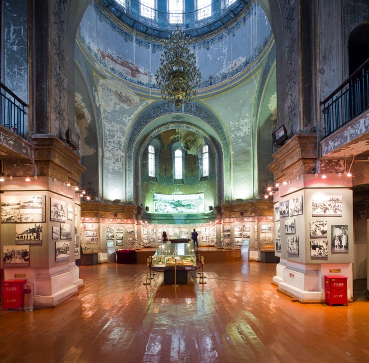 Interior of Harbin Museum of Architecture showing ornate domed ceiling with chandelier and exhibition displays.
