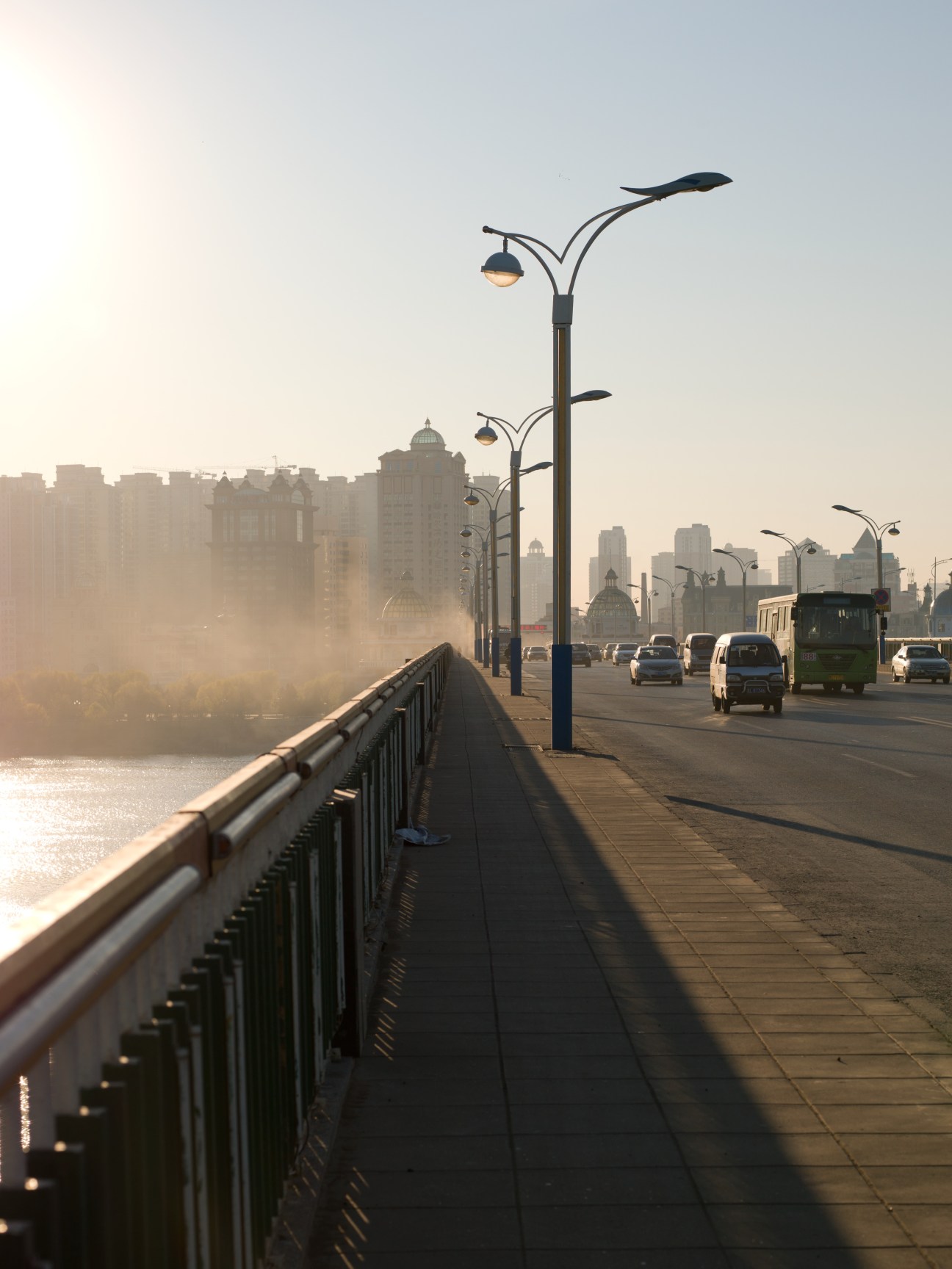 Songhua River Expressway Bridge with street lamps, traffic, and Harbin's skyline shrouded in mist.