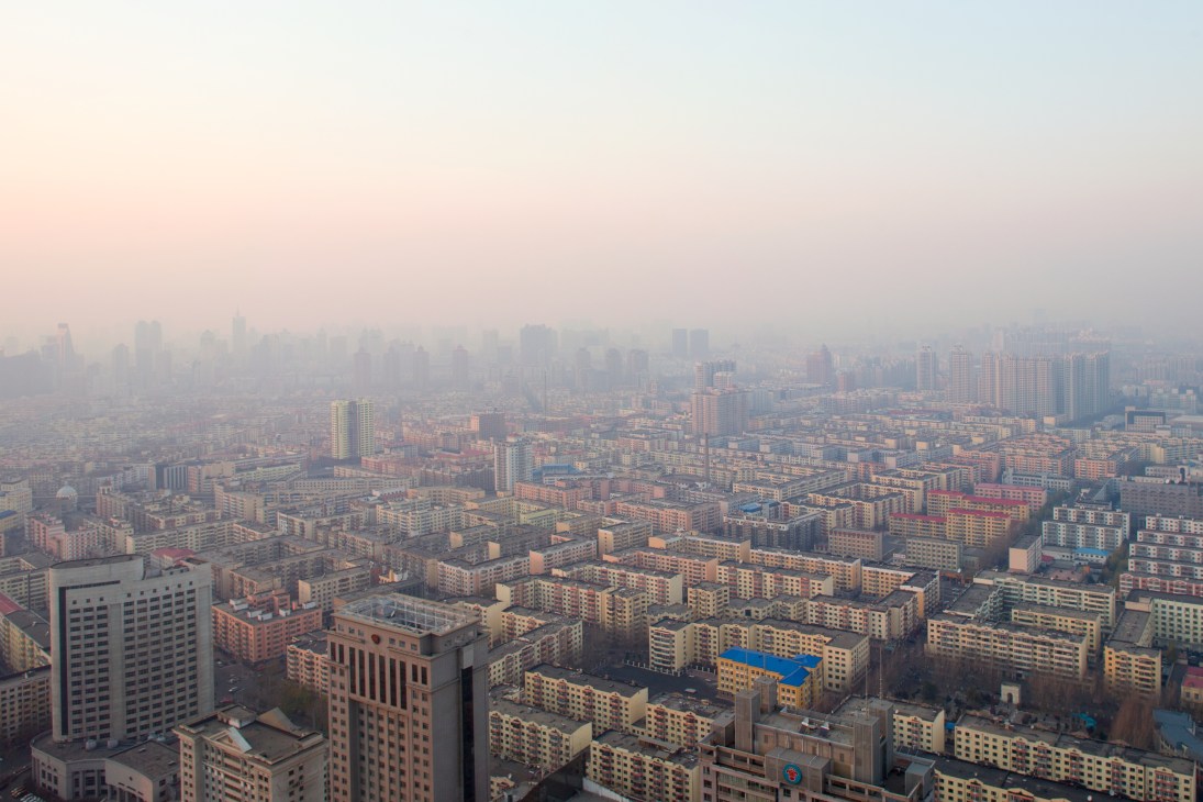 Aerial view of sprawling downtown Harbin cityscape with numerous residential and office tower blocks extending to the horizon under hazy sky.
