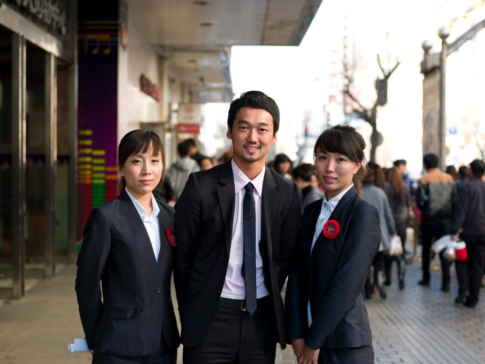 Three Grand Shopping Centre staff members in business attire pose on Guogeli Street in Harbin.