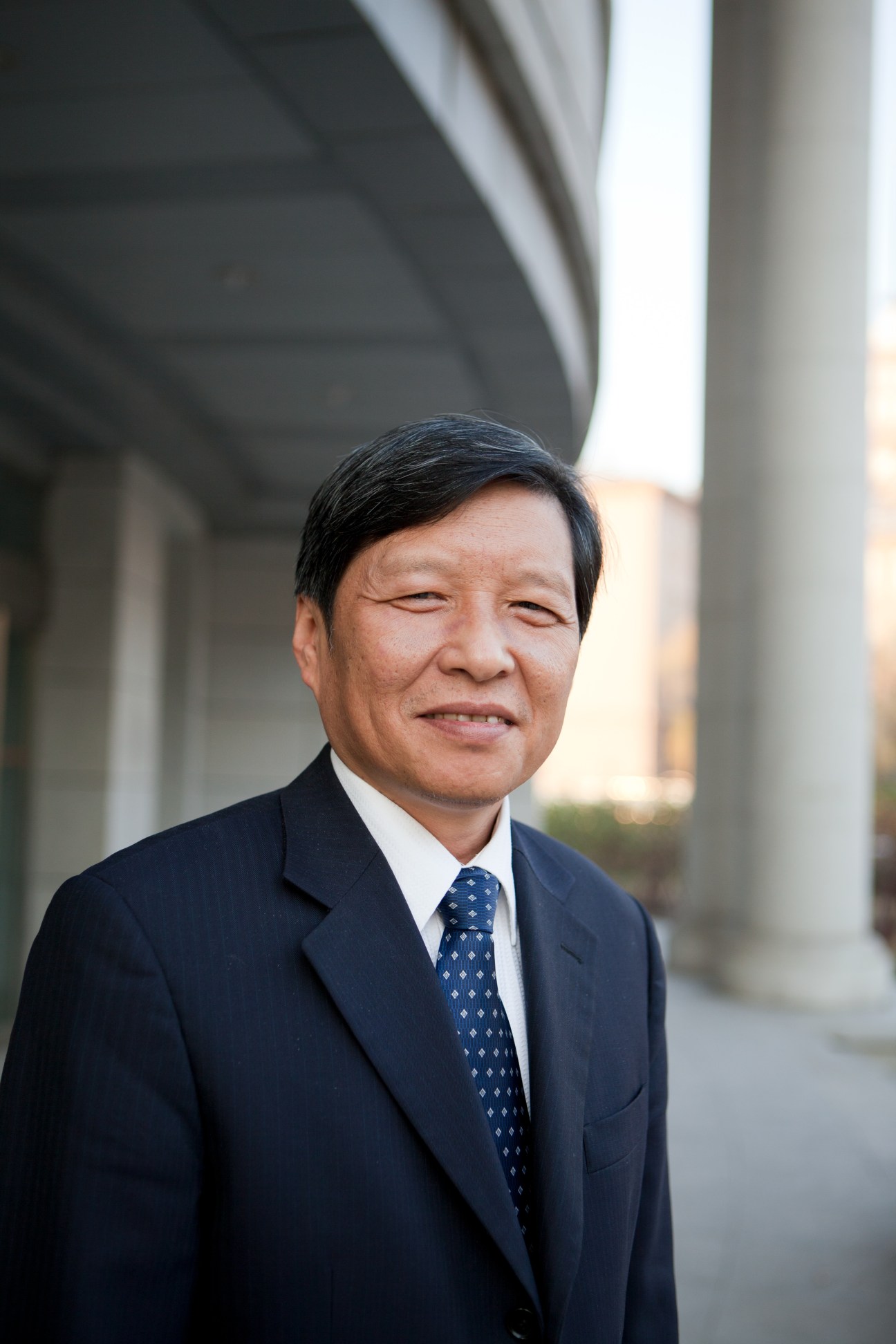 Wang Shuguo, president of Harbin Institute of Technology, in a dark suit and blue tie standing under a concrete overhang.