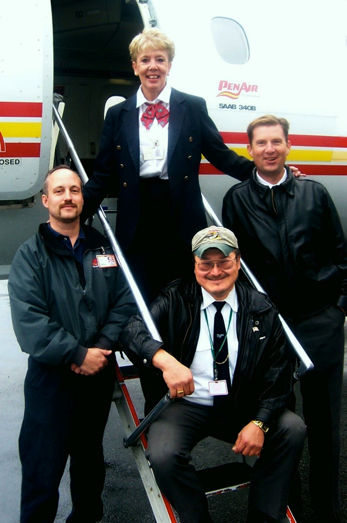 PenAir staff members posing by a SAAB 340 aircraft with the airline's red and yellow livery.