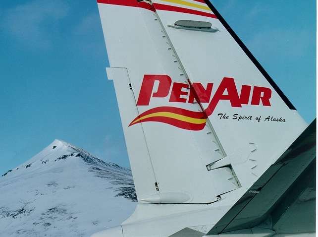 PenAir aircraft tail with red and yellow striping and snow-covered mountain in background.